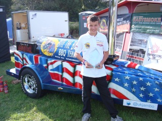 Jamie stands in front of the BBQ with his award 